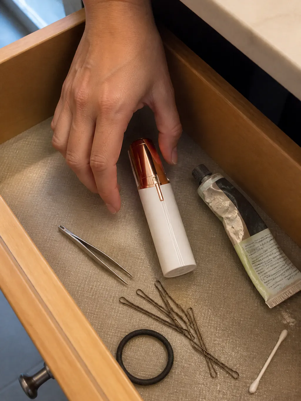The trimmer resting beside tweezers and a wax strip on a bathroom counter