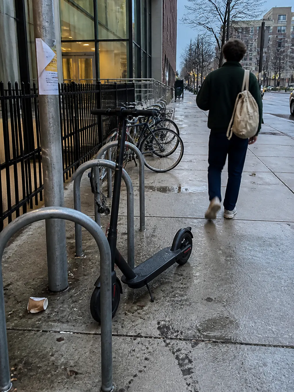 Electric scooter parked at a public bike rack at dusk, rider walking away