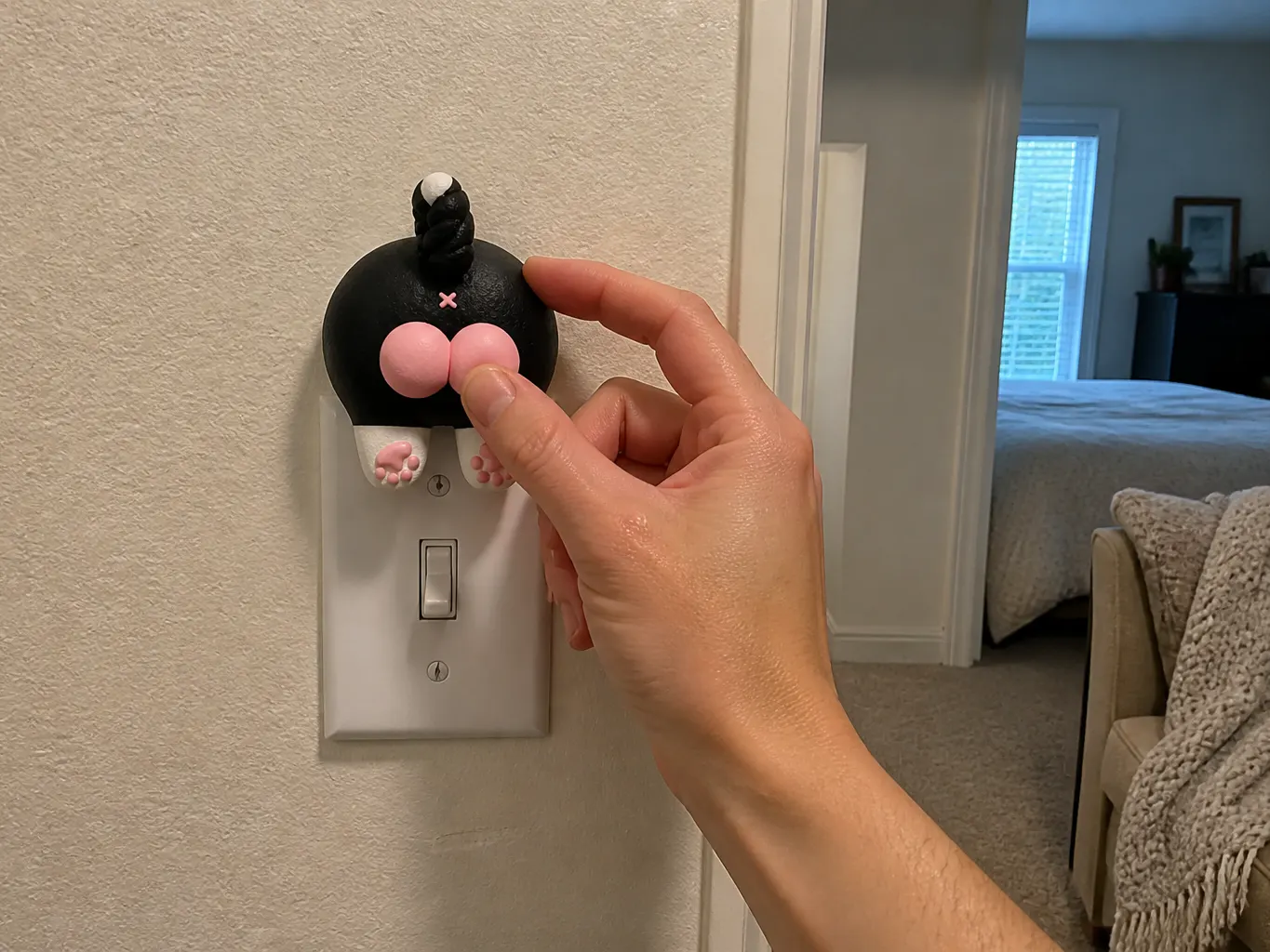A bare hand fitting the sculpted animal cover over an existing wall switch plate