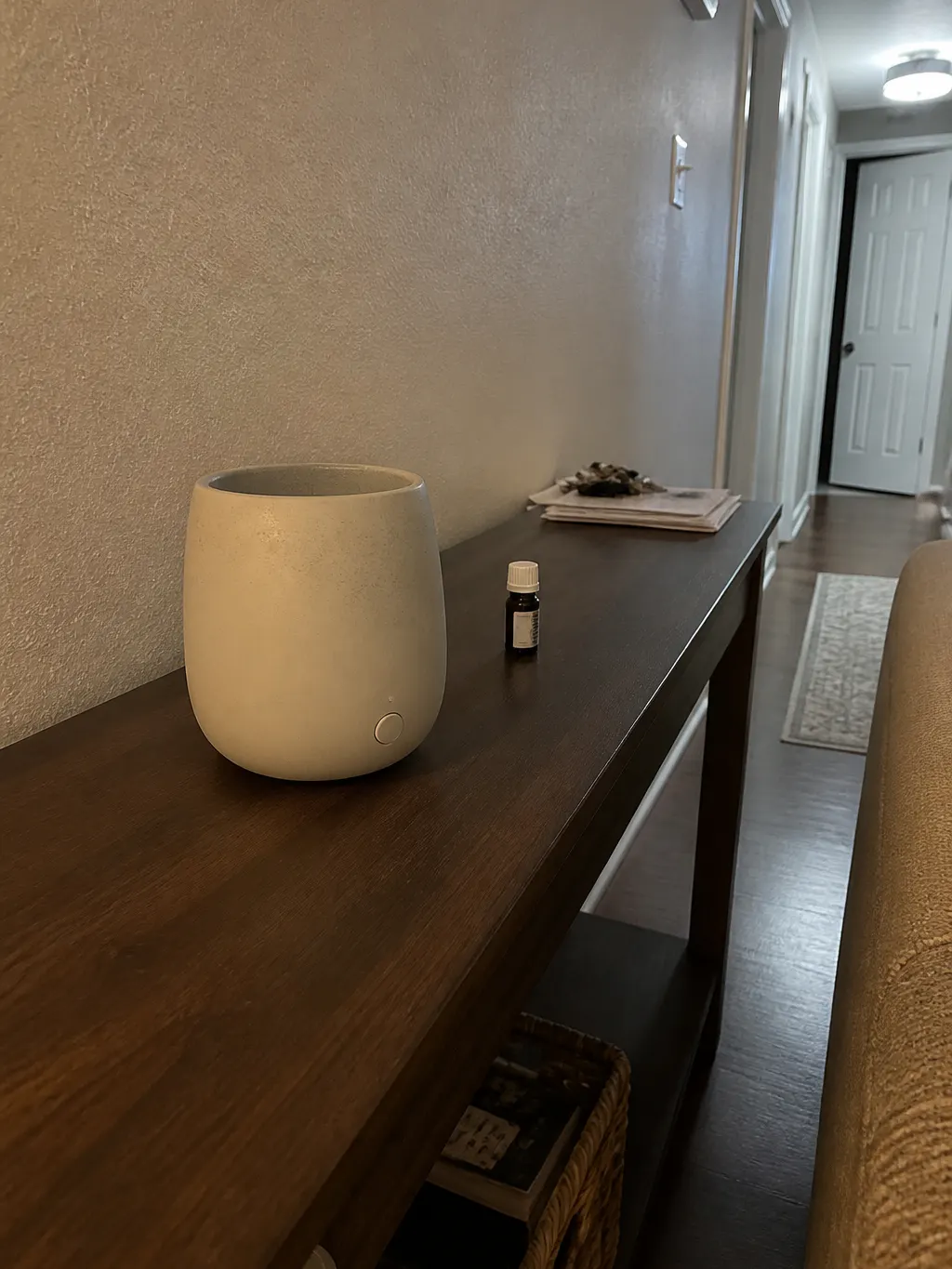 An empty diffuser on a console table beside a tiny oil vial in a dim room
