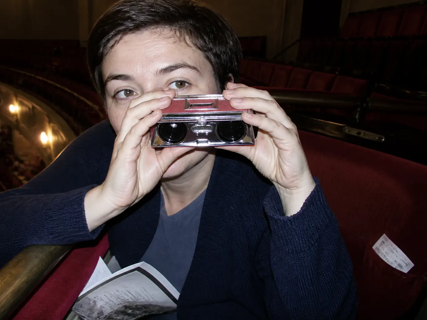 The opened opera glass resting on a folded playbill on a balcony seat