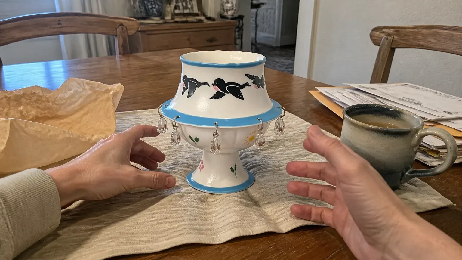 The ceramic pedestal cup newly set down on a wooden console in late afternoon light