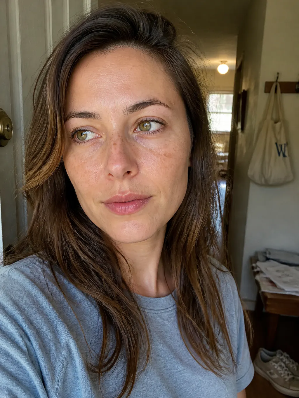 A woman with a bare face and natural freckles stepping outside into daylight