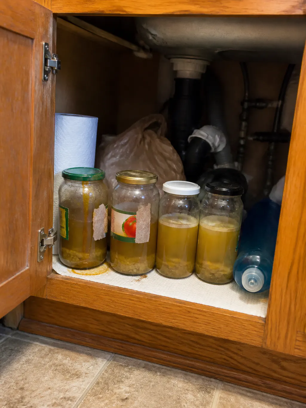 A heavy Dutch oven of cooled brown cooking oil pushed to the back of a cold stove, with mismatched grease jars on the shelf behind it