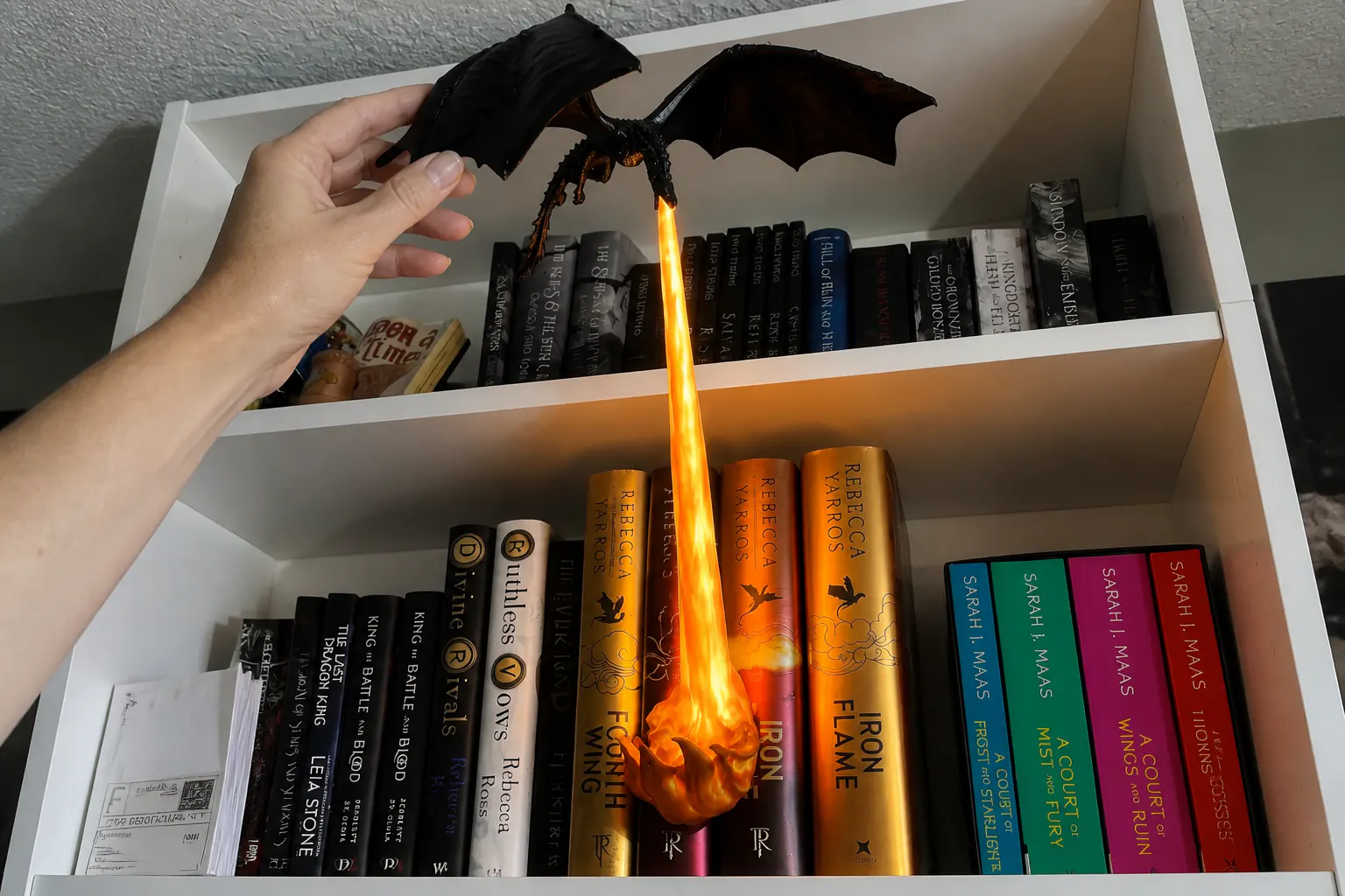 The dragon guardian on a shelf next to real book spines with a hand for scale