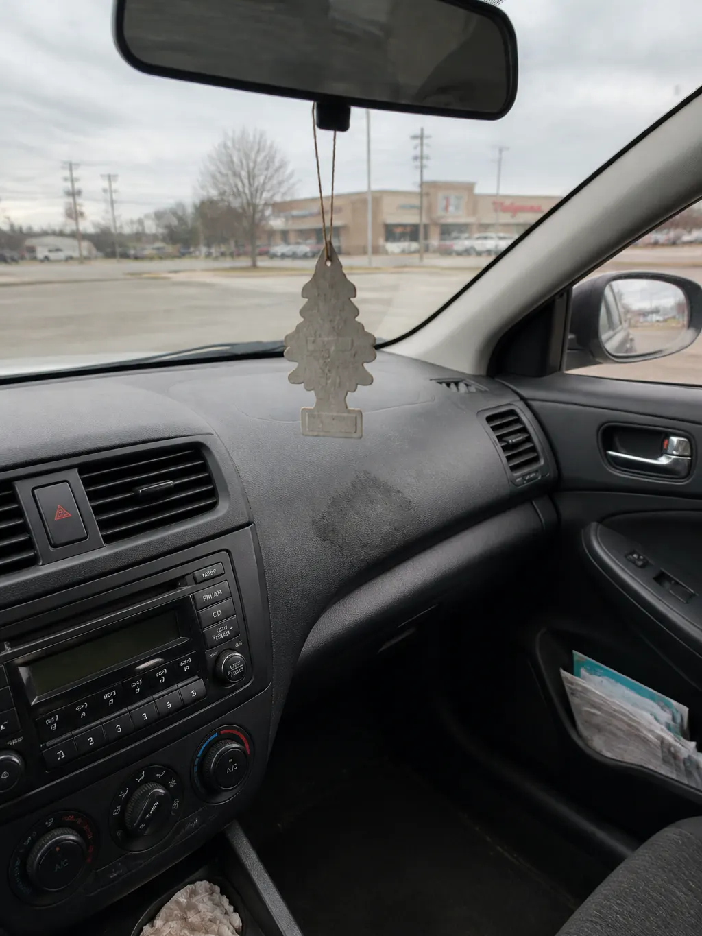A faded cardboard air freshener and an oil-wet felt vent clip resting against a car dashboard