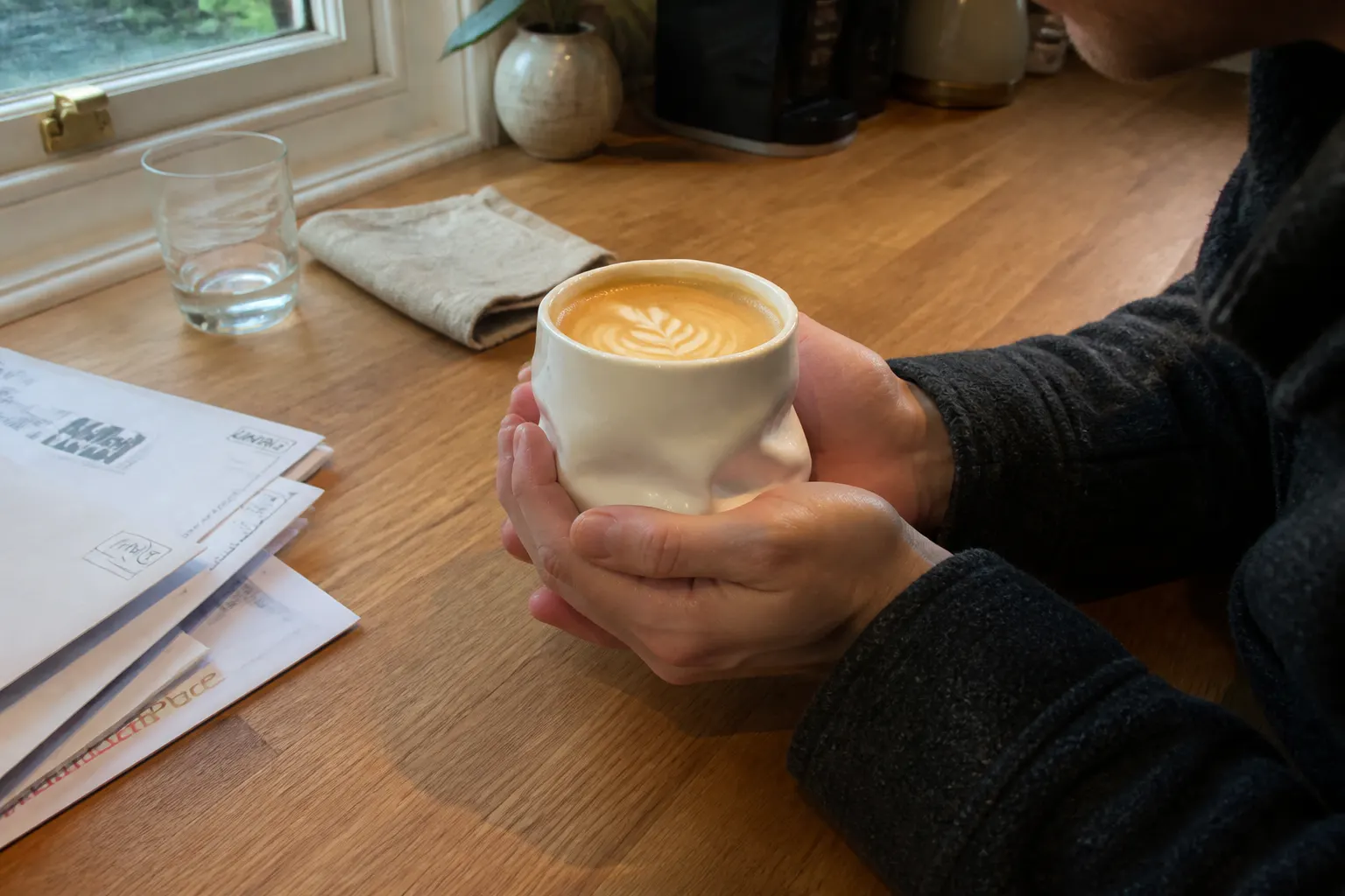 Hands cradling the handleless ceramic sack mug in soft morning light