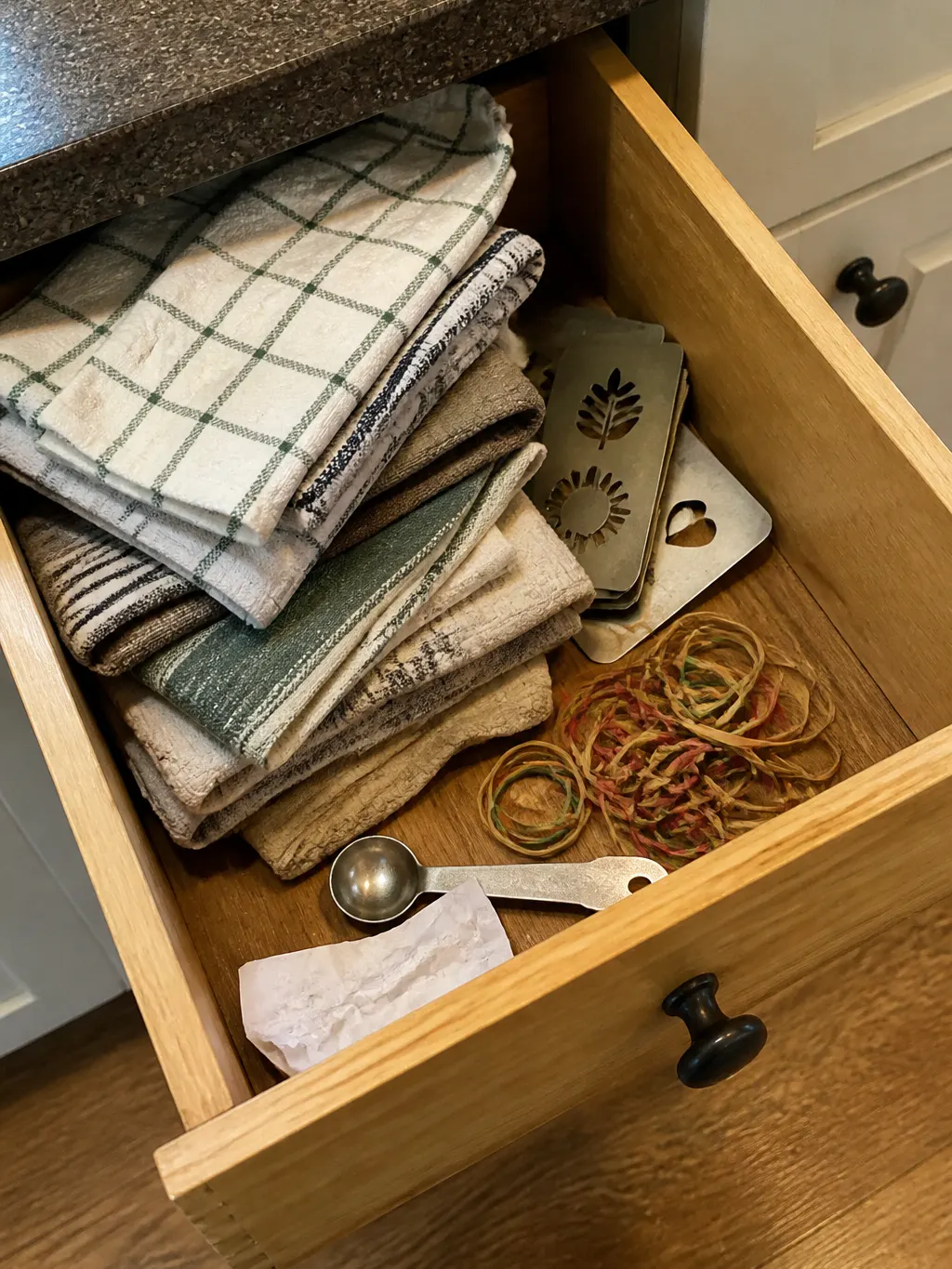 A half-open kitchen drawer with unused flat stencil discs beside a tea towel