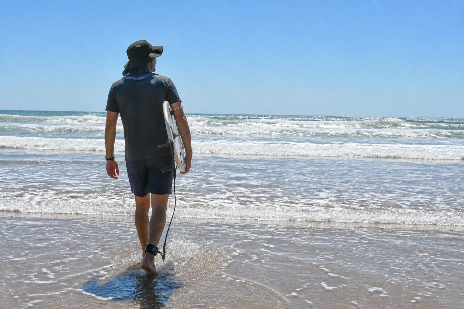 Confident surfer heading into the water wearing the Ventra hat